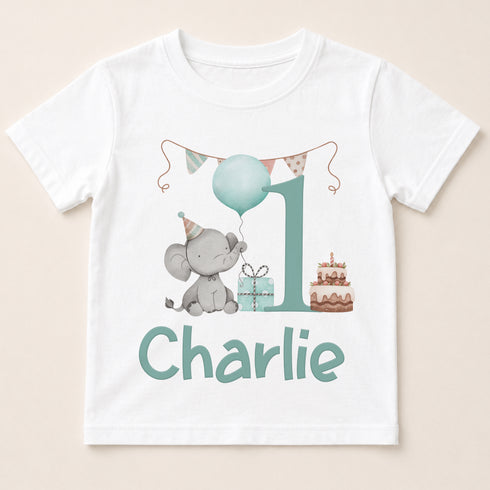 A white t-shirt with a graphic design featuring a gray elephant holding a blue balloon, a gift box, and a birthday cake. The text " Charlie" is displayed below the design.