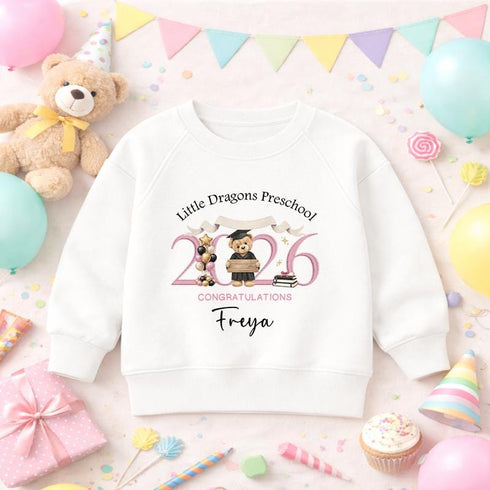 White children’s sweatshirt featuring a personalised pink 2026 teddy bear preschool graduation design with a nursery name and child’s name.