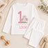 Personalised 1st birthday girl outfit with pink number 1, pretty daisy flower design, happy birthday text and custom name, shown on bib, vest, t-shirt, pyjamas and sleepsuit.
