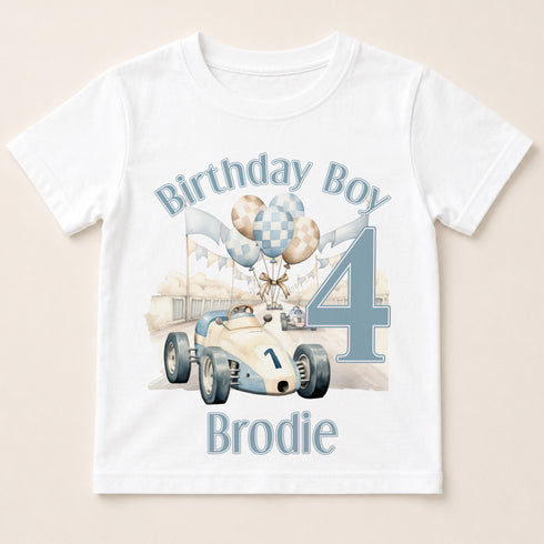 A white t-shirt with a graphic design featuring a race car and balloons, along with the text "Birthday Boy Brodie" and the number "4".