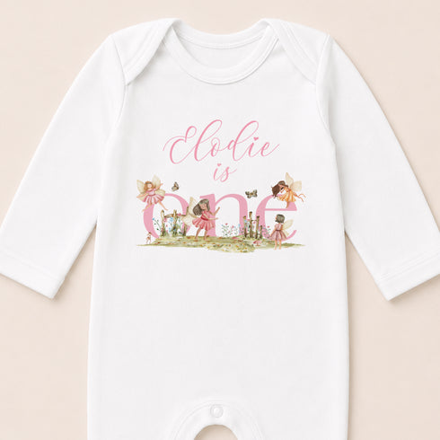 A white onesie with the text "Eodie is one" and illustrations of fairies and butterflies.