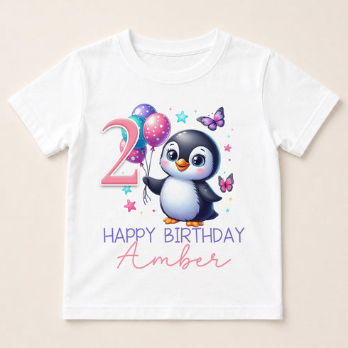 A white t-shirt with a cartoon penguin and colorful balloons, along with the text "2 HAPPY BIRTHDAY AMBER" printed on it.