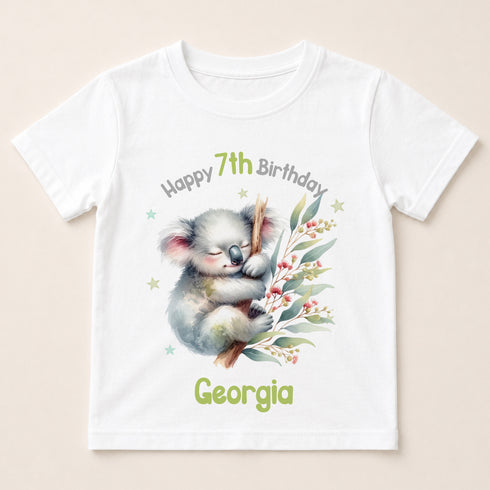 A white t-shirt with a printed design featuring a koala bear and some greenery. The text on the t-shirt reads "Happy 7th Birthday Georgia".