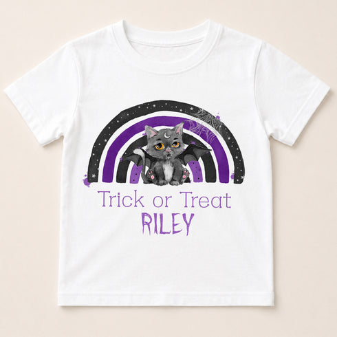 A white t-shirt with a graphic design featuring a cat and a rainbow. The cat is depicted as a bat-like creature, and the rainbow has purple and black colors. The text below the design says "Trick or Treat Riley".