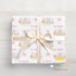 A gift box wrapped with a white ribbon and featuring a repeating pattern of butterflies and the name "Amelia" printed on it.