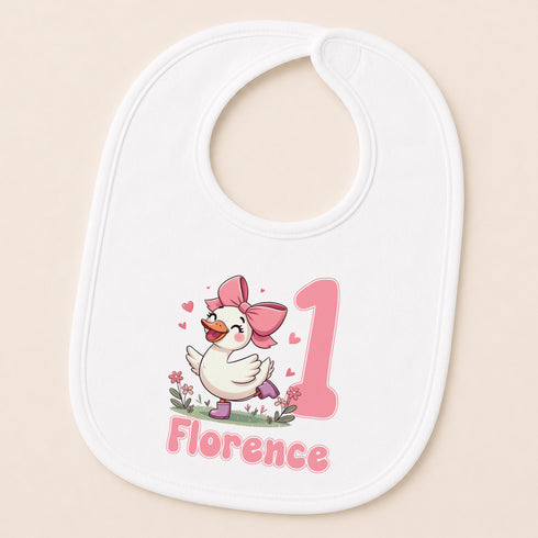 A white bib with a cartoon image of a duck wearing a pink bow and the name "Florence" printed on it.