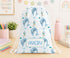 A white drawstring bag with a pattern of blue dolphins and sea creatures printed on it, sitting on a desk surrounded by various school supplies and a rainbow-themed wall decoration.