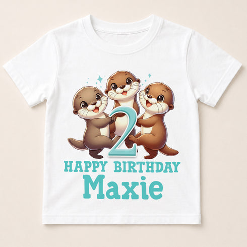 A white t-shirt with a cartoon image of three otters and the number "2" on it, along with the text "Happy Birthday Maxie".
