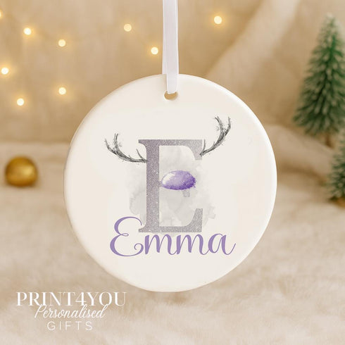 A white ornament with a purple letter "E" and a purple antler design, hanging on a string.