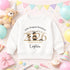 White children’s sweatshirt with a personalised gold 2026 teddy bear nursery graduation design, displayed on a colourful celebration background with balloons and bunting.