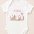 A white baby onesie with a personalized text and illustrations related to a first birthday celebration.