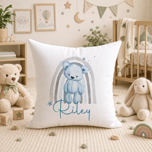 A white pillow with a blue bear and a rainbow design, surrounded by stuffed animals and toys in a nursery setting.