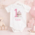 Personalised 1st birthday girl outfit with pink number 1, cute cupcake design, happy birthday text and custom name, shown on sleepsuit, t-shirt, vest, pyjamas and bib.