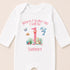 A white onesie with a printed design on it, featuring a pink number 1, a blue dolphin, and various marine life. The text on the onesie says "When I wake up I will be 1 Summer".