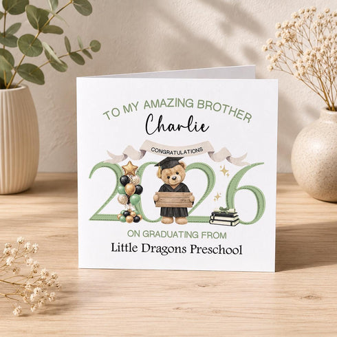 Personalised preschool graduation card with sage green 2026 numbers, graduate teddy bear, balloons, books and custom nursery wording.