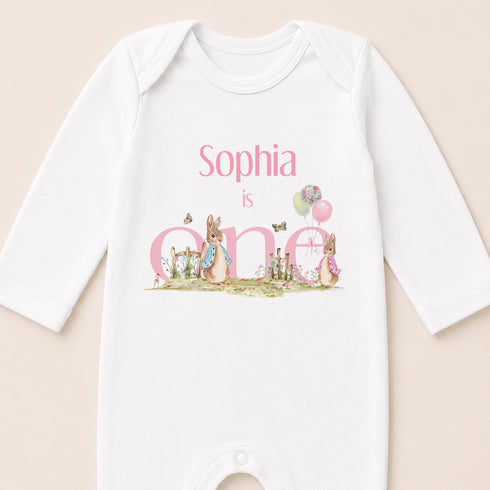 A white onesie with a personalized text and illustrations related to a baby's first birthday.