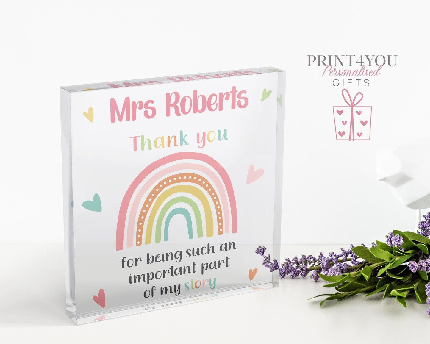 Clear freestanding acrylic block printed with 'Mrs Roberts, Thank you for being such an important part of my story' beside a pastel rainbow design, standing on a white desk.