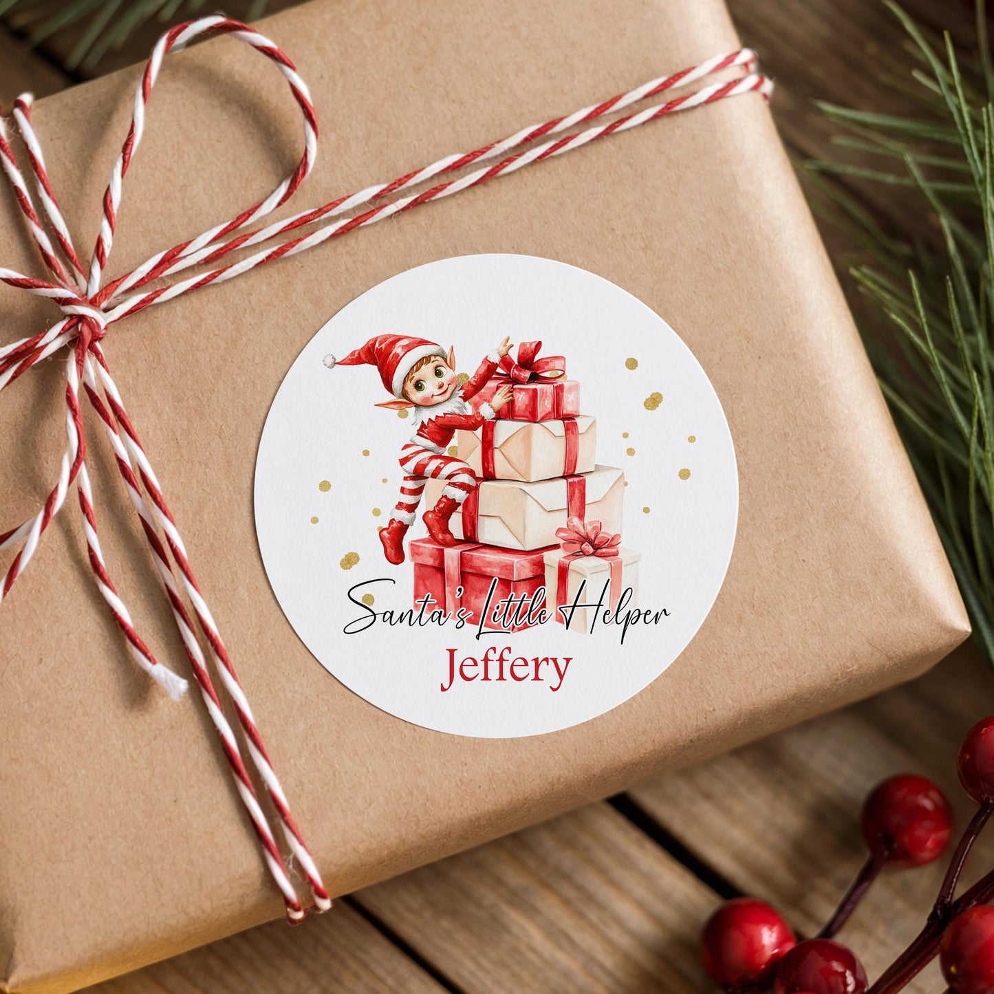 Personalised Santa's Little Helper elf sticker with custom name on a stack of wrapped Christmas gifts