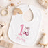 Personalised 1st birthday girl outfit with pink number 1, cute cherry bow design, happy birthday text and custom name, shown on bib, vest, sleepsuit, t-shirt and white pyjamas.