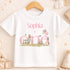 A white t-shirt with a personalized text and illustrations, including a rabbit and balloons, is displayed on a wooden hanger.
