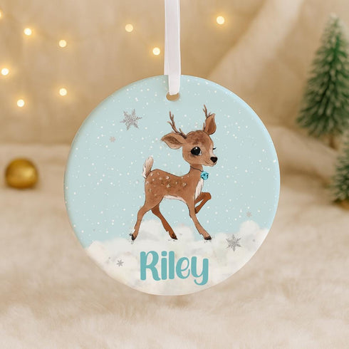 A round ornament featuring a cartoon deer with the name "Riley" written on it, set against a snowy background with stars.