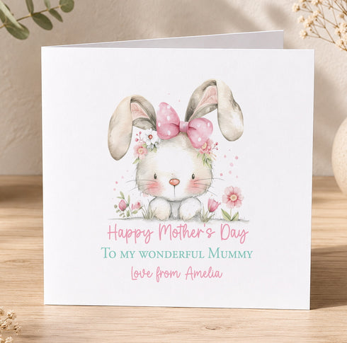 A white greeting card with a cute bunny wearing a pink bow and surrounded by flowers, with the text "Happy Mother's Day To my wonderful mummy Love from Amelia" printed on it.
