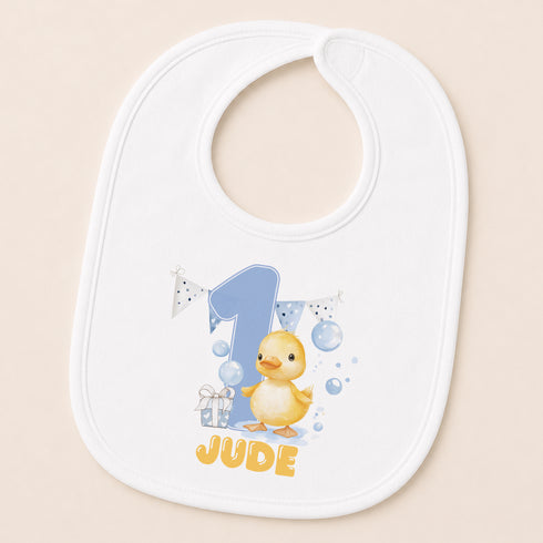 A white baby bib with a cartoon image of a yellow duck and the name "JUDE" printed on it.