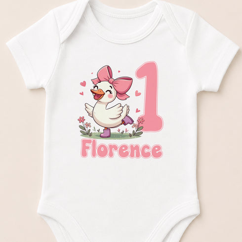 A white baby onesie with a cartoon image of a duck wearing a pink bow and the name "Florence" printed on it.