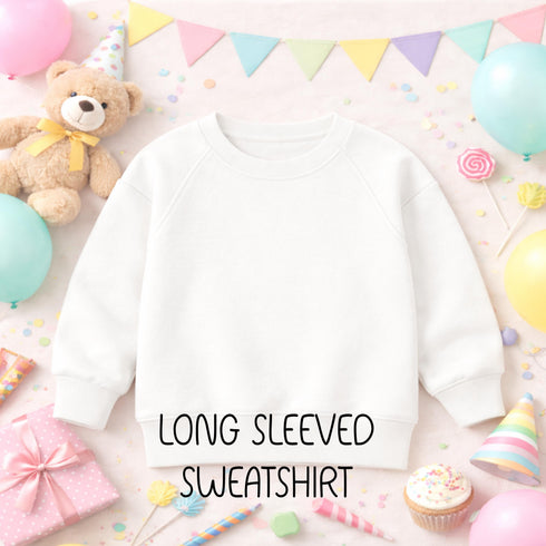 A white long-sleeved sweatshirt is displayed among a variety of colorful party decorations, including balloons, a teddy bear, and a cupcake.