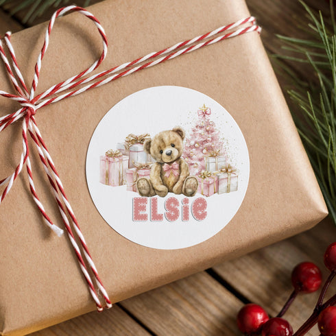 A brown gift box wrapped with a red and white striped ribbon, featuring a teddy bear and Christmas presents. The name "ELSIE" is written on a circular sticker or label attached to the gift box.
