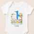 A white baby onesie with a blue number 1 and a graphic of an elephant, lion, and tiger.