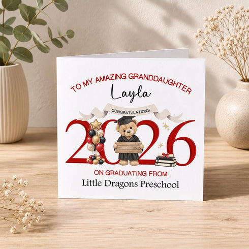 Personalised preschool graduation card with red 2026 numbers, graduate teddy bear, balloons, books and custom nursery wording.