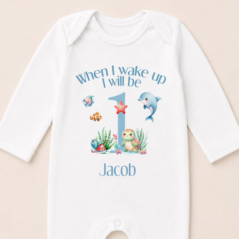 A white onesie with a personalized message and illustrations of marine animals, including a dolphin, starfish, and fish, printed on it.