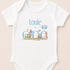 A white baby onesie with the text "Louie is one" and illustrations of rabbits and balloons.