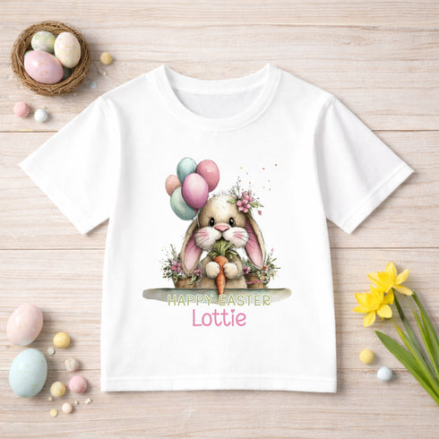 A white t-shirt with a bunny graphic and the text "Happy Easter Lottie" printed on it, surrounded by Easter decorations such as eggs, flowers, and a basket of eggs.