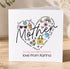 A handmade card with a heart-shaped design featuring various colorful elements, such as flowers, butterflies, and a rainbow, along with the word "Mother" written in a stylized font.