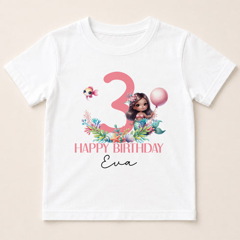 A white t-shirt with a graphic design featuring a mermaid character, a number 3, and a balloon. The text below the design reads "Happy Birthday Eva".