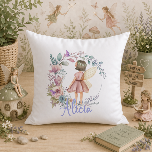 A white pillow with a floral design and the name "Alicia" printed on it, surrounded by various fairy figurines, a mushroom, and a book.