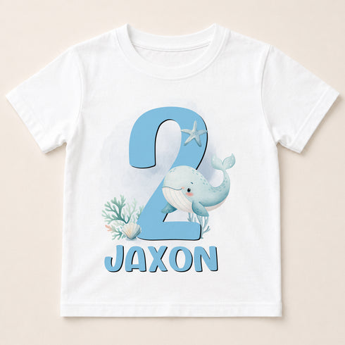 A white t-shirt with a blue whale and starfish design, along with the text "JAXON" printed on it.
