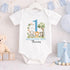 Personalised 1st birthday boy outfit with blue number 1, safari animals, elephant, lion, zebra, tree and custom name, shown on bib, vest, sleepsuit, t-shirt and white pyjamas.