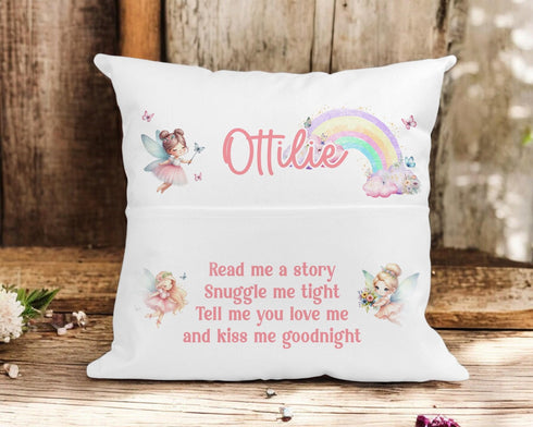 "A decorative pillow with a white background, placed on a wooden surface. The pillow features whimsical illustrations of fairies and butterflies, along with a colourful rainbow and clouds. The text on the pillow reads: 'Childs name, Read me a story, Snuggle me tight, Tell me you love me, and kiss me goodnight