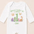 A white onesie with a personalized message and illustrations of various animals, including a sun, dragon, and dinosaur, printed on it.