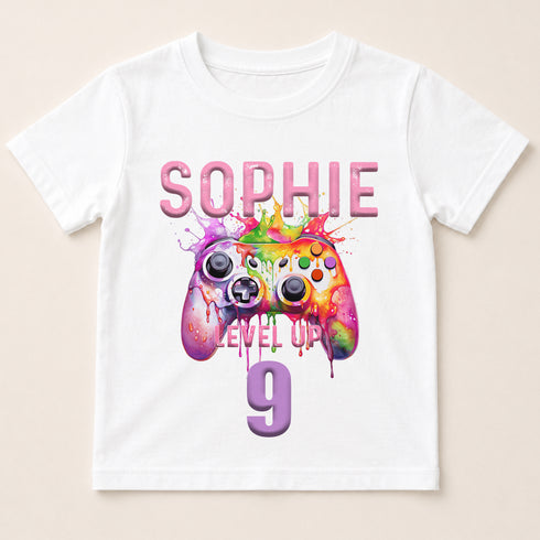 A white t-shirt with a graphic design featuring a colorful game controller and the text "SOPHIE LEVEL UP 9" printed on it.