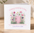 A white card with a pink wooden gate and colorful flowers, along with the text "Happy Mother's Day To the Best Mum in the World Love from Callie".