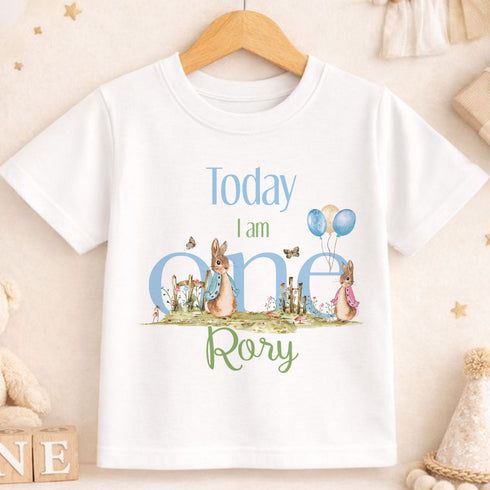 A white t-shirt with a graphic design featuring rabbits and balloons, along with the text "Today I am oneary" printed on it.