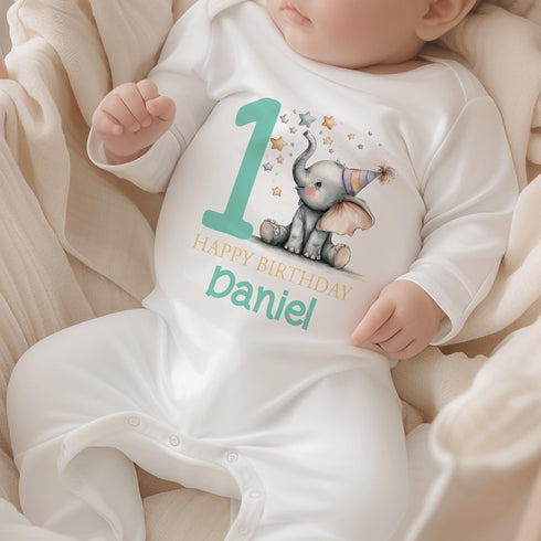 Personalised 1st birthday baby outfit with cute elephant, party hat, stars, teal number 1 and custom name, shown on bib, vest, sleepsuit, t-shirt and white pyjamas.