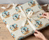 A person's hands are wrapping a gift with a patterned wrapping paper featuring the word "Rodeo" and the number "1st".