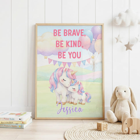 a framed poster with a unicorn and a bunny, along with the text "Be Brave, Be Kind, Be You" and the name " Jessica". The poster is displayed on a white wall, and there are some stuffed animals and books in the foreground.