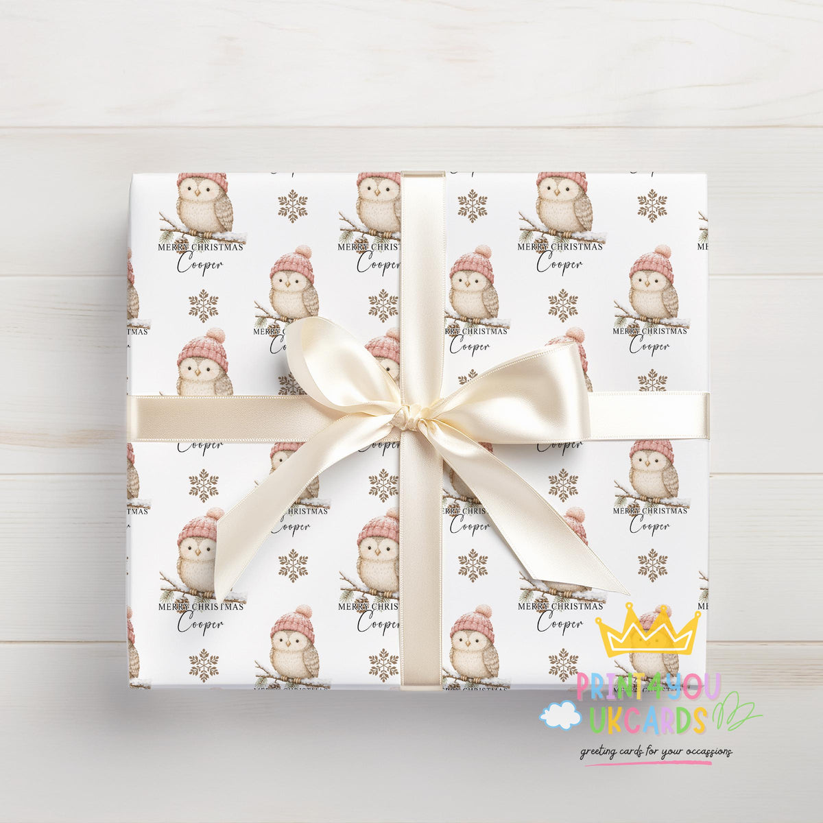 Gift wrapped in owl and snowflake Christmas paper viewed from above, tied with a cream bow.