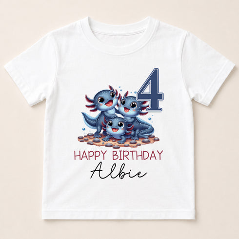A white t-shirt with a graphic design featuring three cartoon axolotls, which are a type of salamander, and the number 4. The text below the design reads "Happy Birthday Albie".